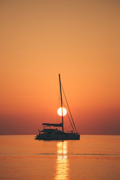 SUNSET COLLECTION Catamarán en el mar con el sol poniéndose detrás de él en un atardecer cálido.